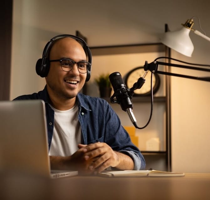 Young Asian content creator recording a podcast in a home studio, using a professional microphone and laptop to livestream an interview—representing modern influencer marketing and digital brand partnerships.